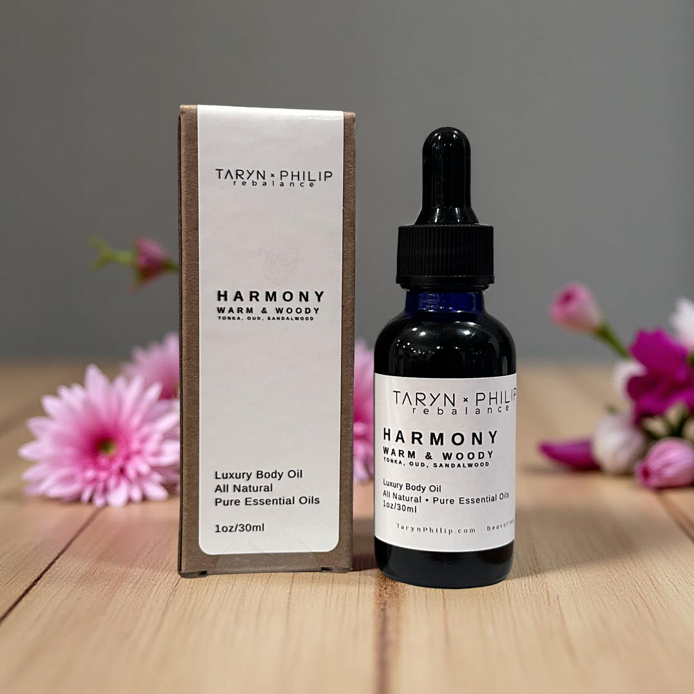Taryn x Philip Rebalancing Harmony body oil bottle and packaging on a wooden surface with flowers.