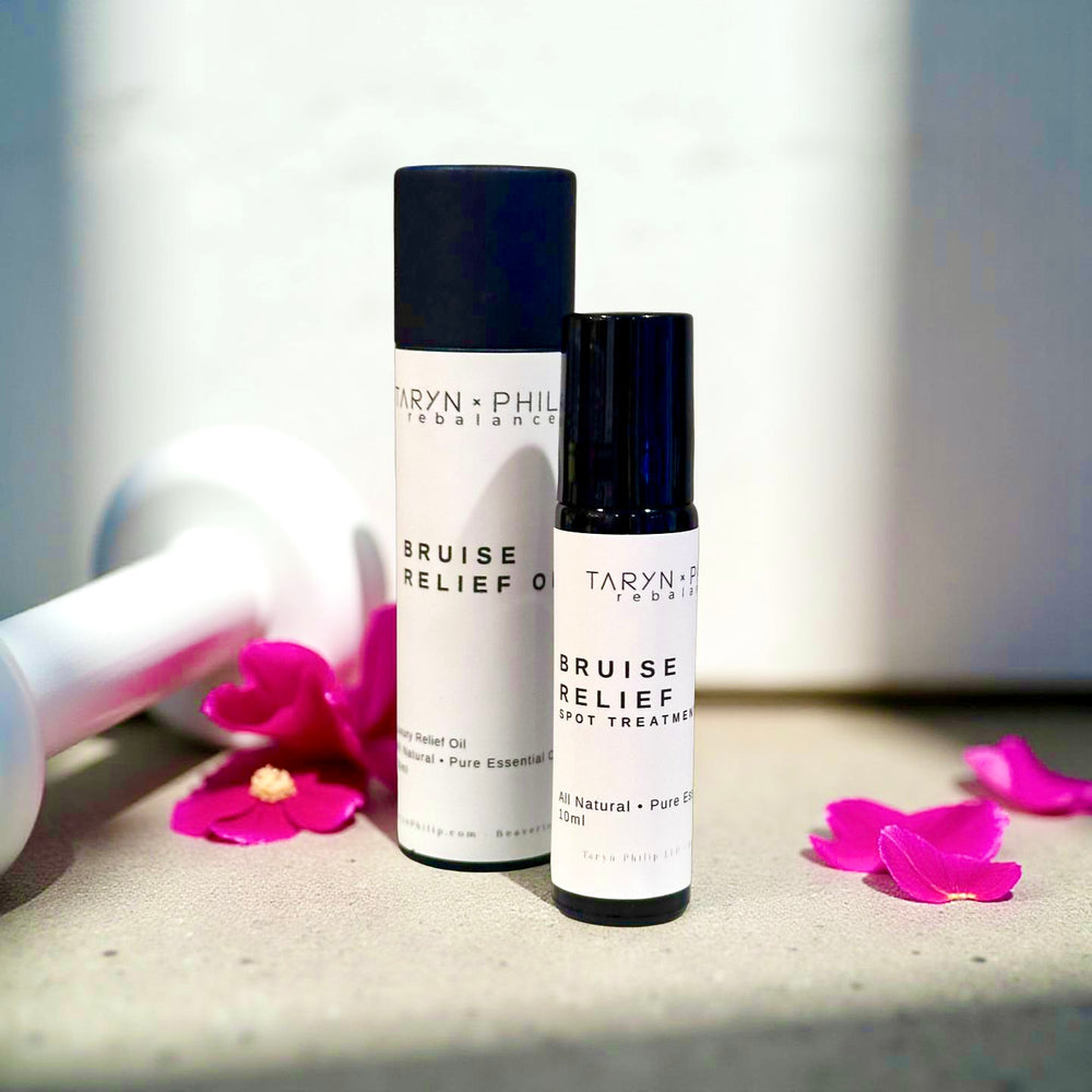 Two bottles of Taryn x Philip Bruise Relief on a surface with pink flowers.