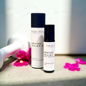 Two bottles of Taryn x Philip Bruise Relief on a surface with pink flowers.
