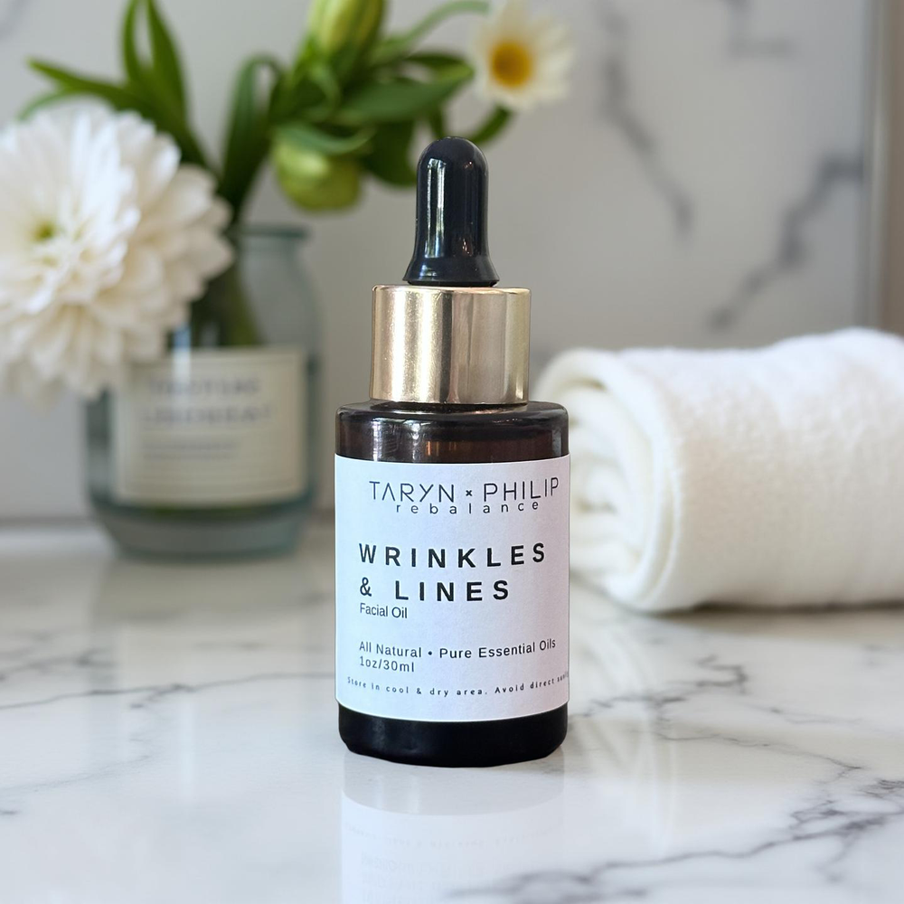 Facial oil bottle labeled 'Wrinkles & Lines' by Taryn x Philip on a marble surface with flowers in the background.