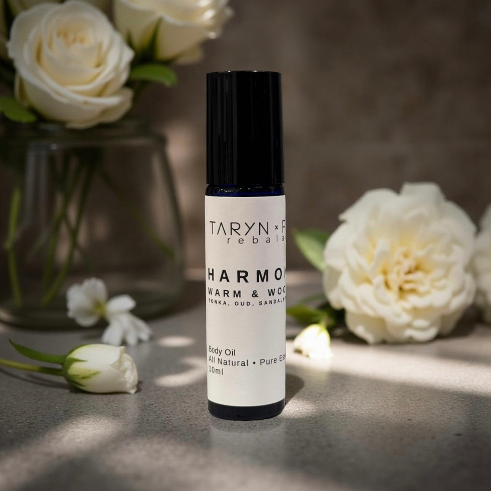 Taryn x Philip Rebalancing Harmony body oil bottle and packaging on a wooden surface with flowers.