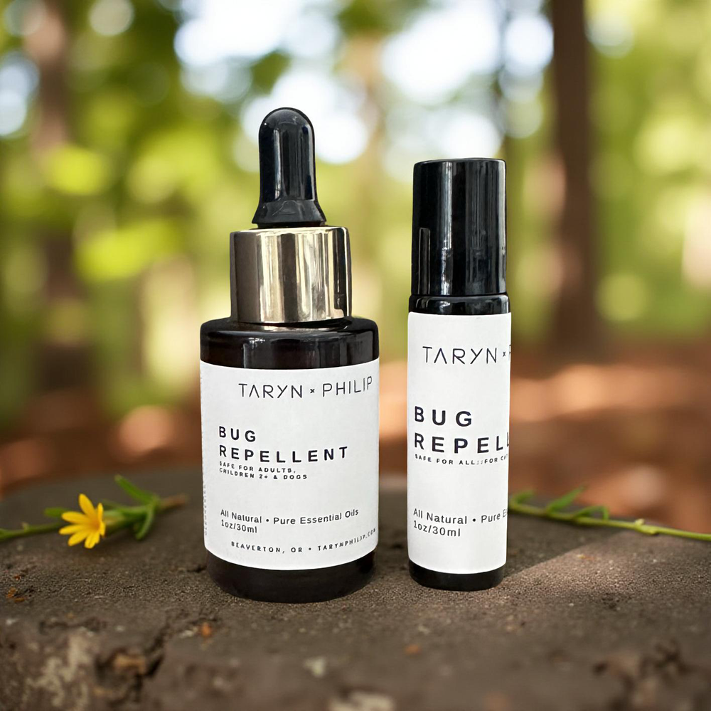 Two bottles of Taryn x Philip bug repellent on a natural background with a flower.
