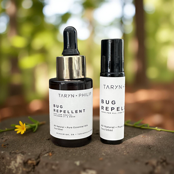 Two bottles of Taryn x Philip bug repellent on a natural background with a flower.